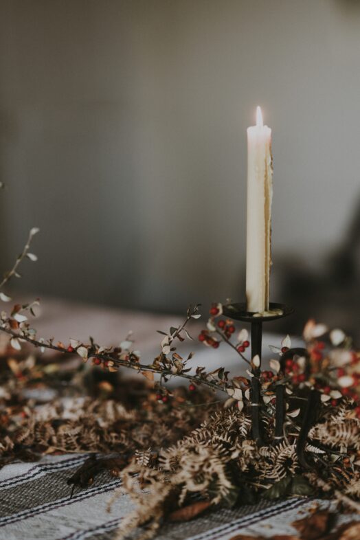 Ett tänt ljus i en ljusstake omgiven av torkade blommor.