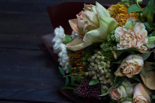 En bukett med olika blommor och gröna blad på ett mörkt bord.